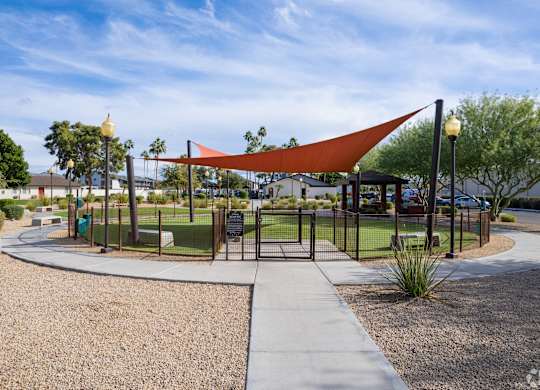 A playground with a red shade structure and a black fence.
