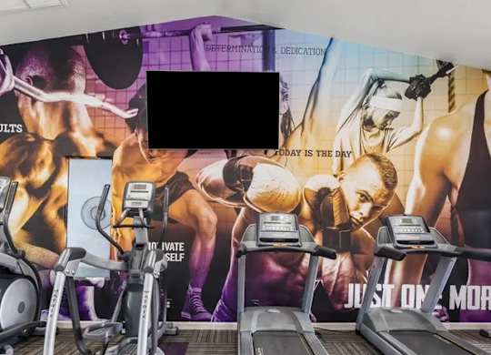 A gym with treadmills and exercise equipment in front of a wall with fitness motivational posters.