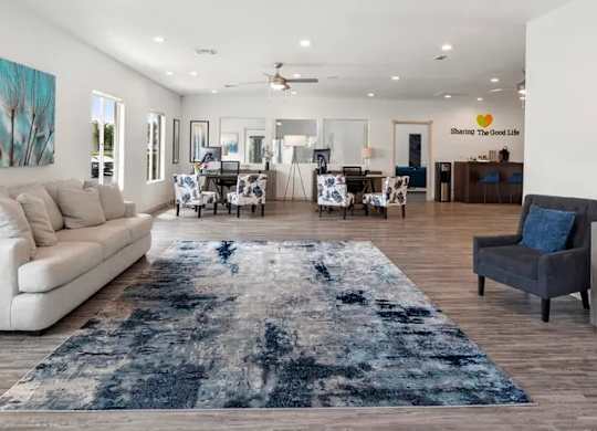 A spacious living room with a rug in the center and a sign that says "Sharing the Good Life".