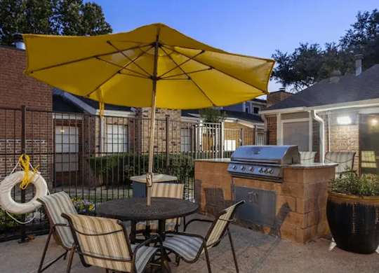 A patio with a table, chairs, and a yellow umbrella.
