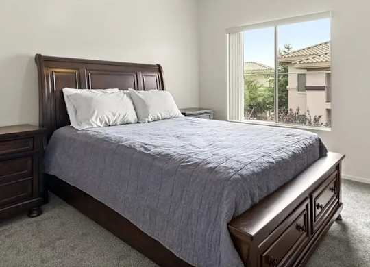 A bedroom with a bed, nightstand, and window.