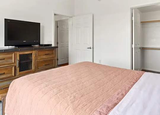 A bedroom with a bed, a television, and a ceiling fan.