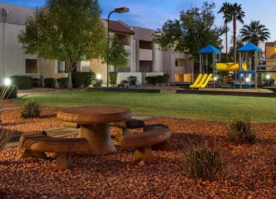 A playground with a slide and a picnic table is lit up at dusk.