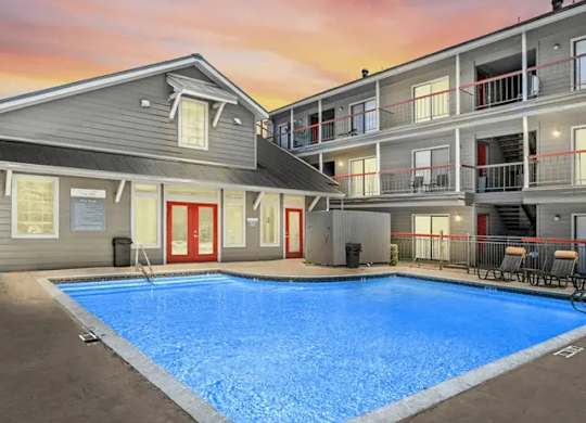 A swimming pool in front of a building with a sunset in the background.