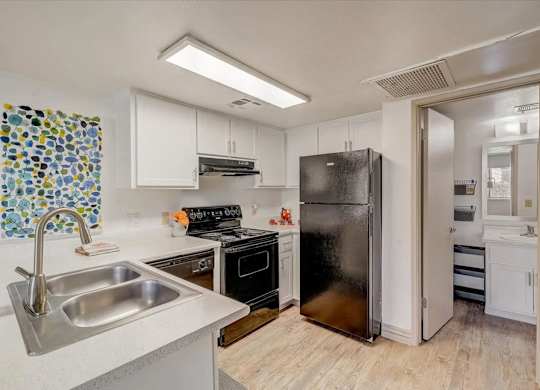 A kitchen with a black refrigerator and a sink with a silver faucet.