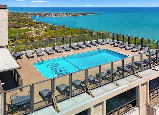 A pool with lounge chairs is surrounded by a balcony railing.