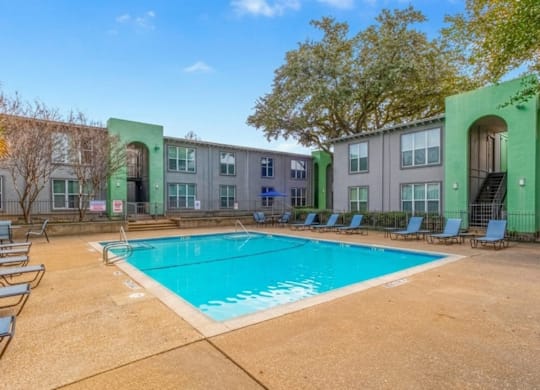 A swimming pool surrounded by chairs and trees in front of a building.