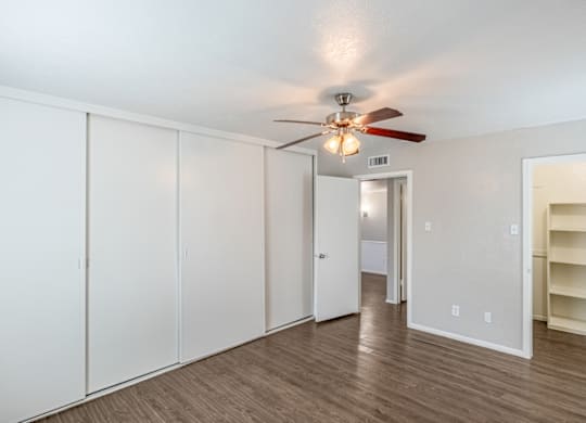 A room with a ceiling fan and a row of white cupboards.