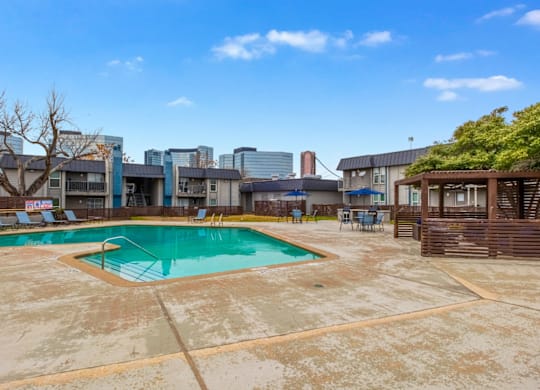 A large outdoor swimming pool surrounded by a concrete patio and buildings in the background.