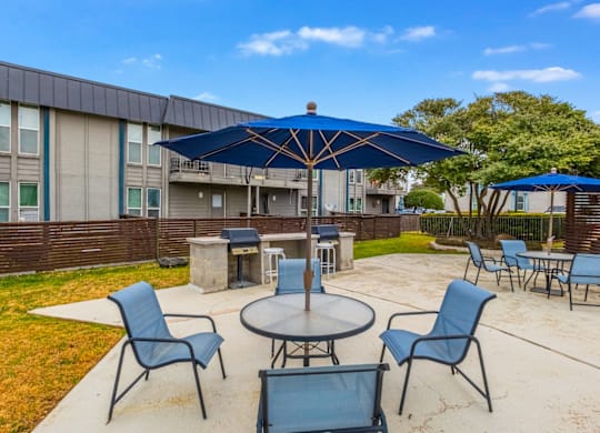 A blue umbrella shades a table and chairs in a courtyard.