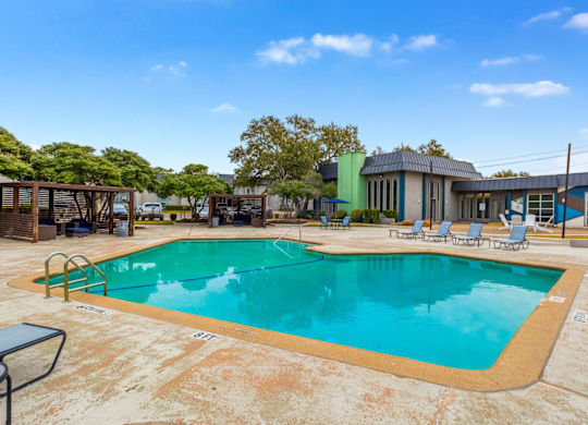 A large outdoor swimming pool surrounded by lounge chairs and trees.