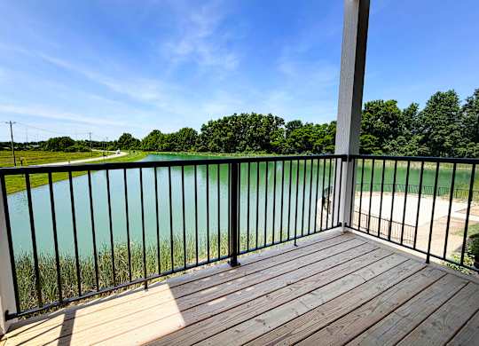 A wooden deck with a black railing overlooks a body of water.