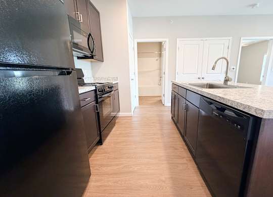 A kitchen with black appliances and wooden floors.