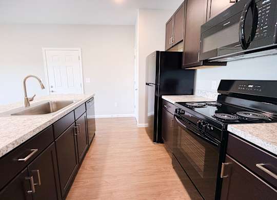 A kitchen with black appliances and wooden floors.