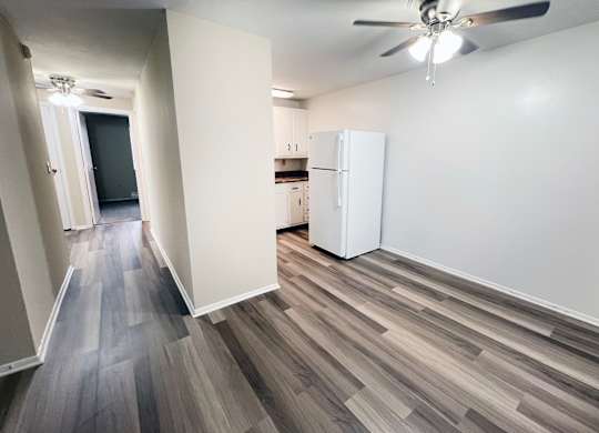 A room with a white fridge and a ceiling fan.