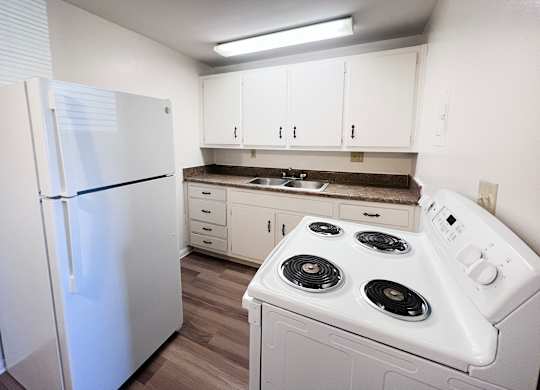 A white refrigerator stands in a kitchen with white cabinets and a white stove.