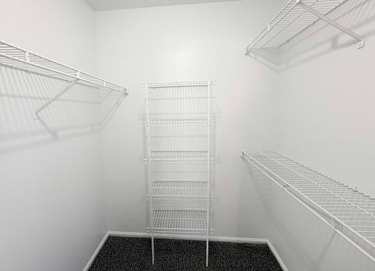 A walk-in closet with white shelving and a black carpeted floor.