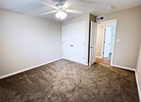 A room with a carpeted floor and a ceiling fan.
