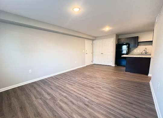 A room with wooden flooring and a kitchenette in the background.