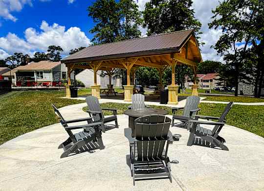 A gazebo with four chairs and a table is surrounded by trees.