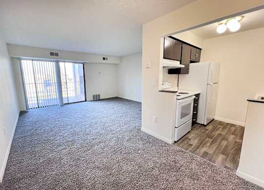 A spacious living area with a kitchenette and a sliding glass door leading to a balcony.