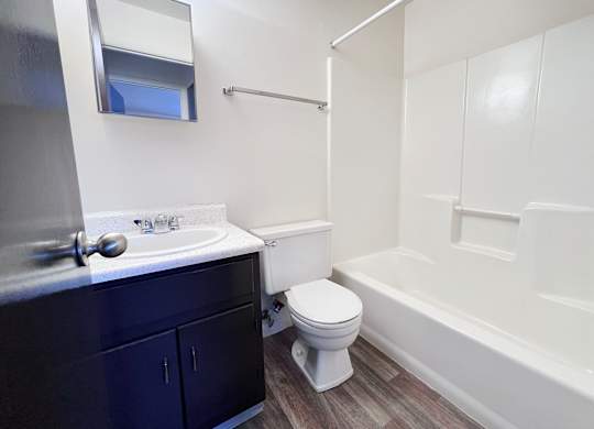 A white toilet sits in a bathroom with a white sink and a white bathtub.