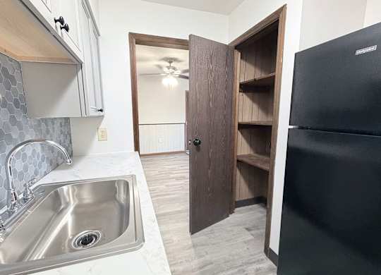 A kitchen with a black refrigerator and a sink with a silver faucet.