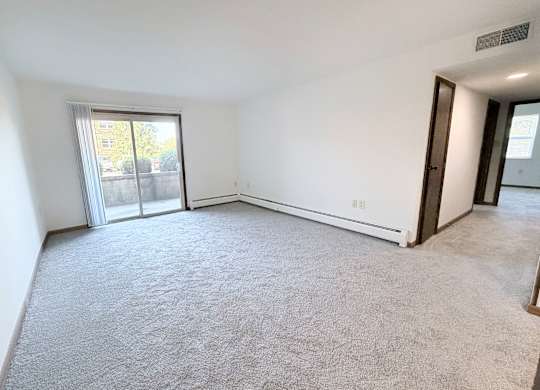 A spacious room with a carpeted floor and sliding glass doors leading to a balcony.