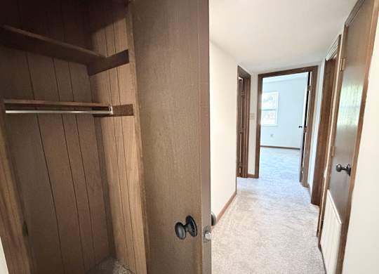 A hallway with a door on the right and a shelf on the left.