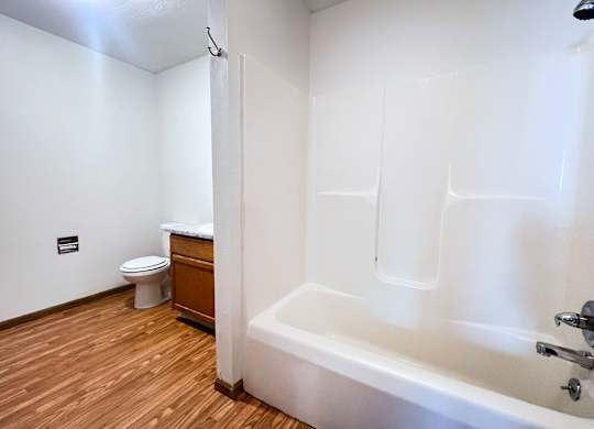 A white bathroom with a wooden floor and a white bathtub.