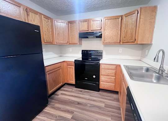A kitchen with a black fridge and wooden cabinets.