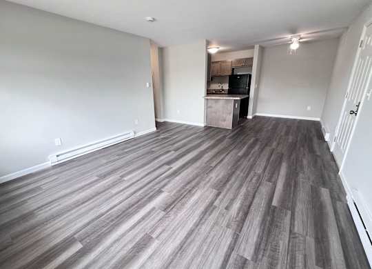 A room with a wooden floor and a kitchen in the background.