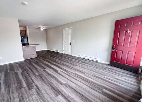 A room with a red door and a wooden floor.