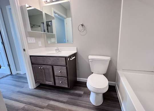 A white toilet sits in a bathroom next to a sink and a bathtub.