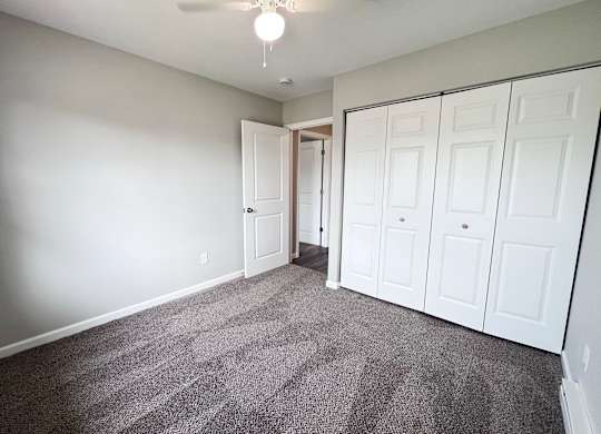 A room with a grey carpet and white cupboards.