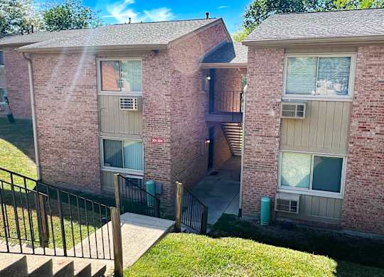 A brick apartment building with a black railing and a green trash can.