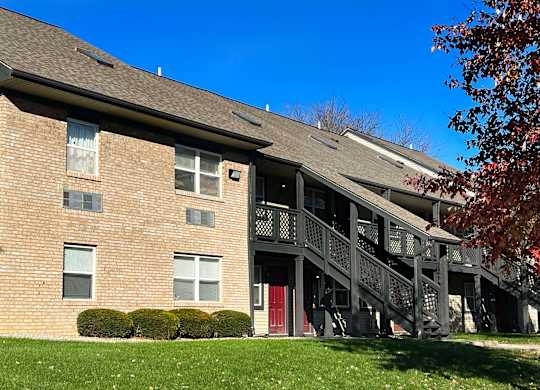 A red door is on the lower level of a multi-story brick building.