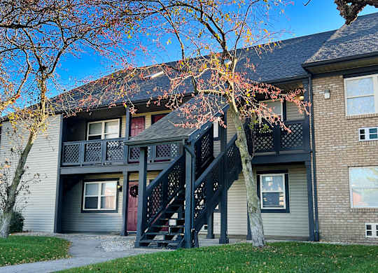 A tree with red leaves is in front of a grey house with a black staircase.