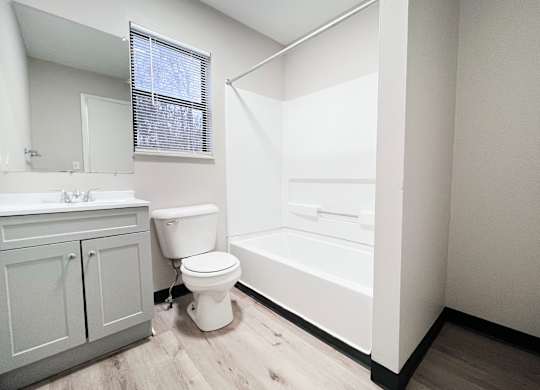 A white toilet sits in a bathroom with a white tub and sink.
