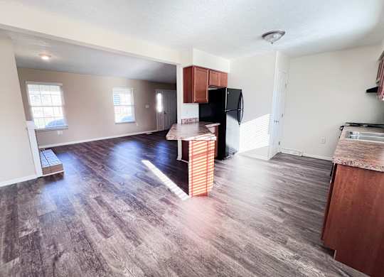 A kitchen area with a black fridge and wooden cabinets.