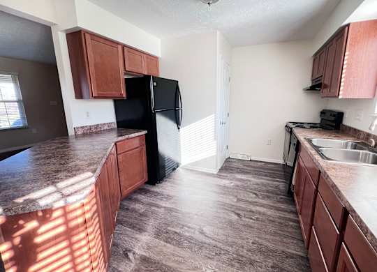 A kitchen with brown cabinets and a black refrigerator.