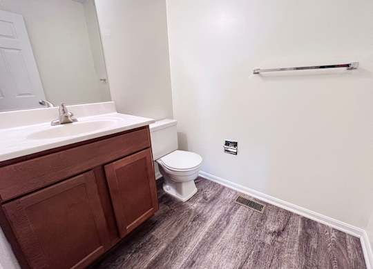 A bathroom with a toilet, sink, and wooden flooring.