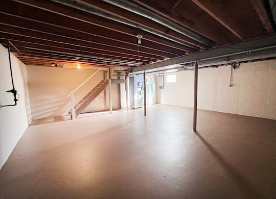 A spacious attic room with wooden beams and a staircase.