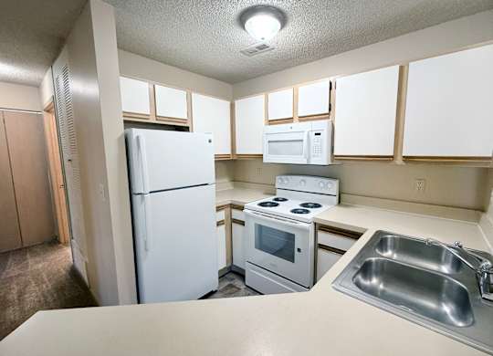 A kitchen with a white refrigerator, microwave, oven, and sink.