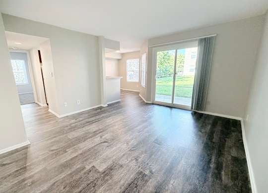 A spacious room with wood flooring and sliding glass doors leading to a green outdoor area.