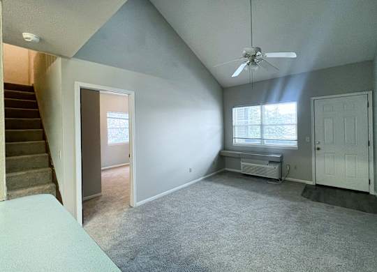 A room with a staircase on the left and a window with a bench on the right.