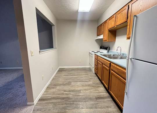 A kitchen with a white refrigerator, wooden cabinets, and a window.