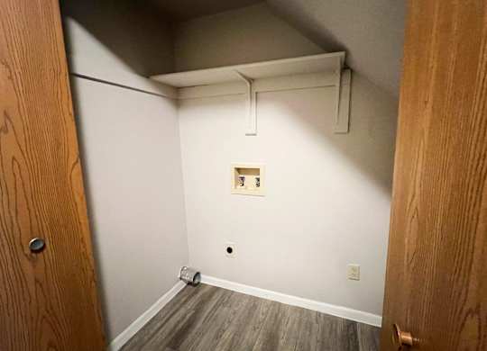 A room with a wooden floor and a white wall with a small square on it.
