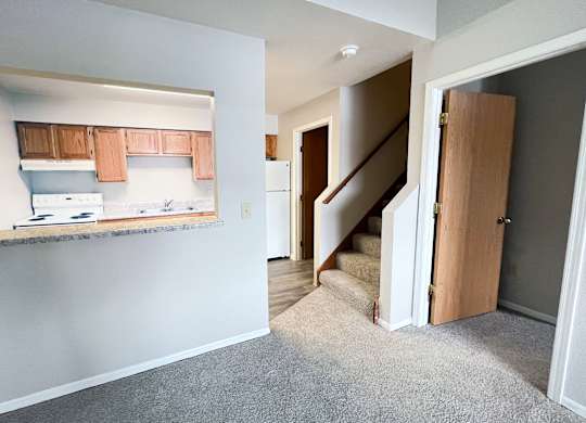 A kitchen with white appliances and wooden cabinets is seen from the living room.