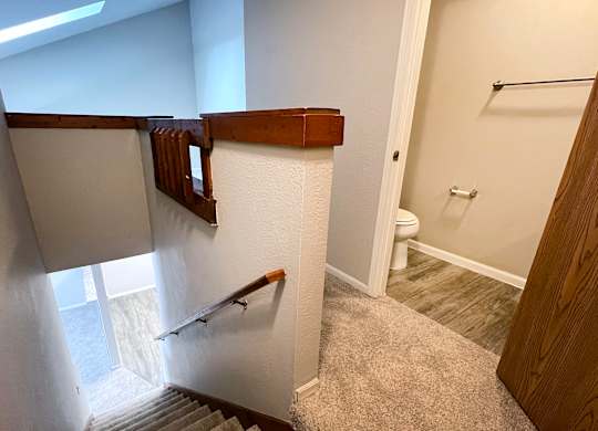 A hallway with a staircase and a toilet in the background.